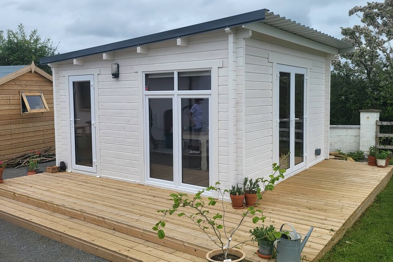A white log cabin with a deck outside it.